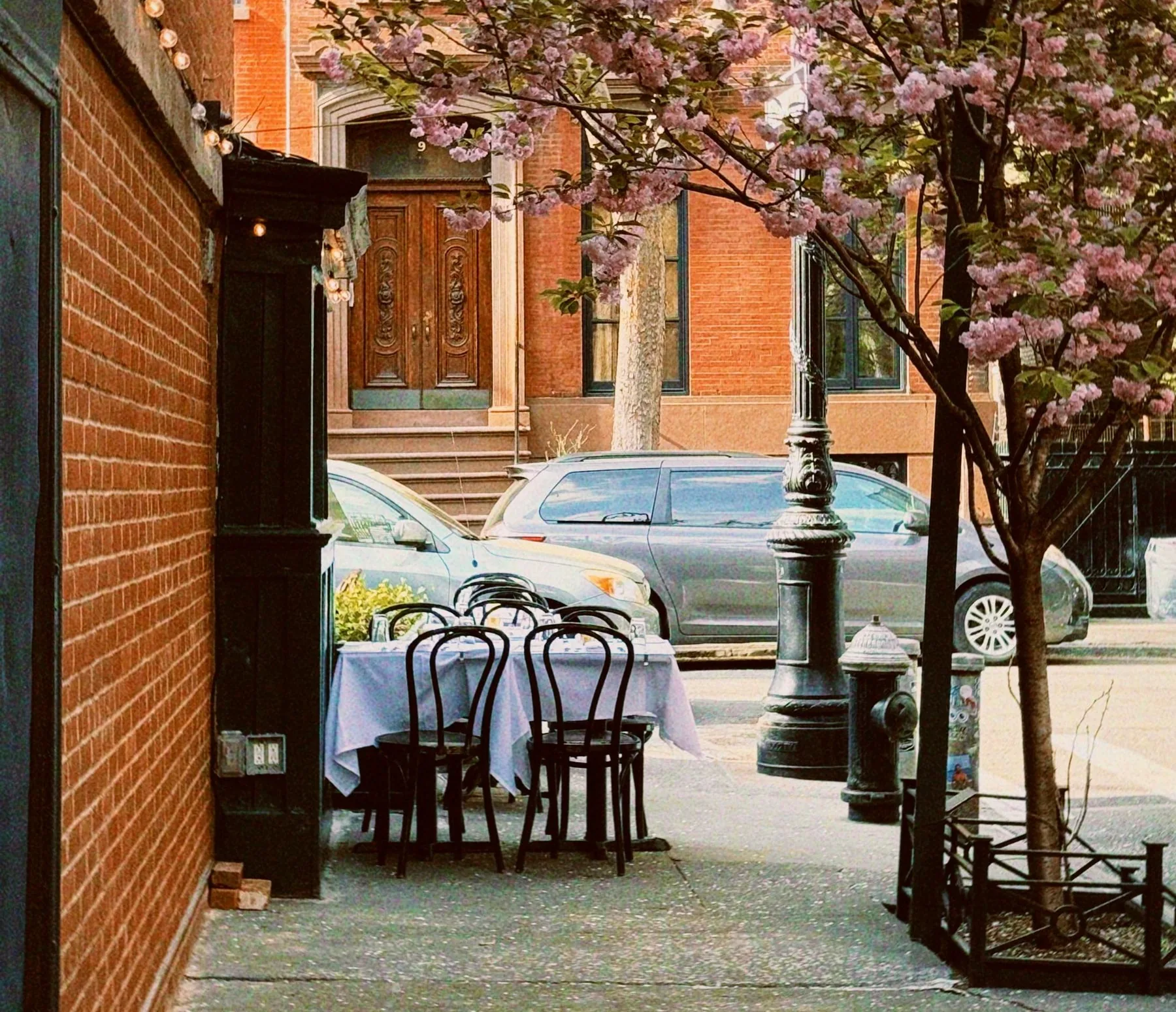 Outdoor café tables and chairs beside a Greenwich Village sidewalk under a flowering tree.