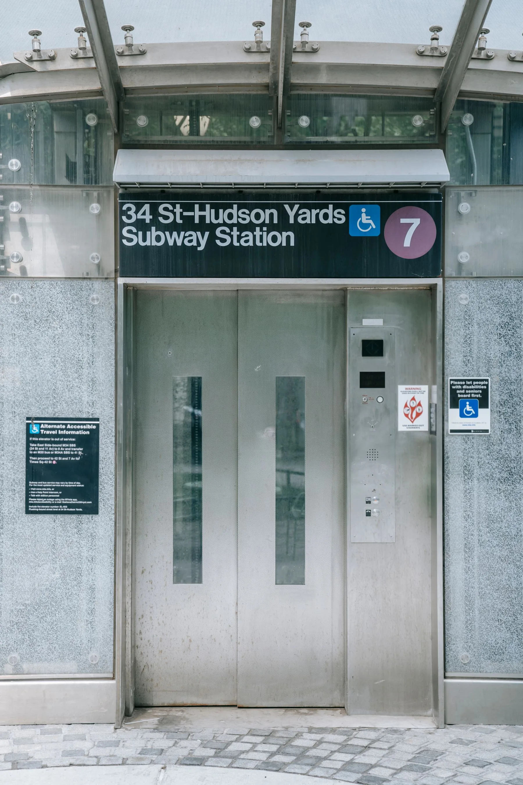 Street-level elevator doors at 34 St–Hudson Yards Subway Station in New York, beneath a wheelchair symbol and 7 train sign.
