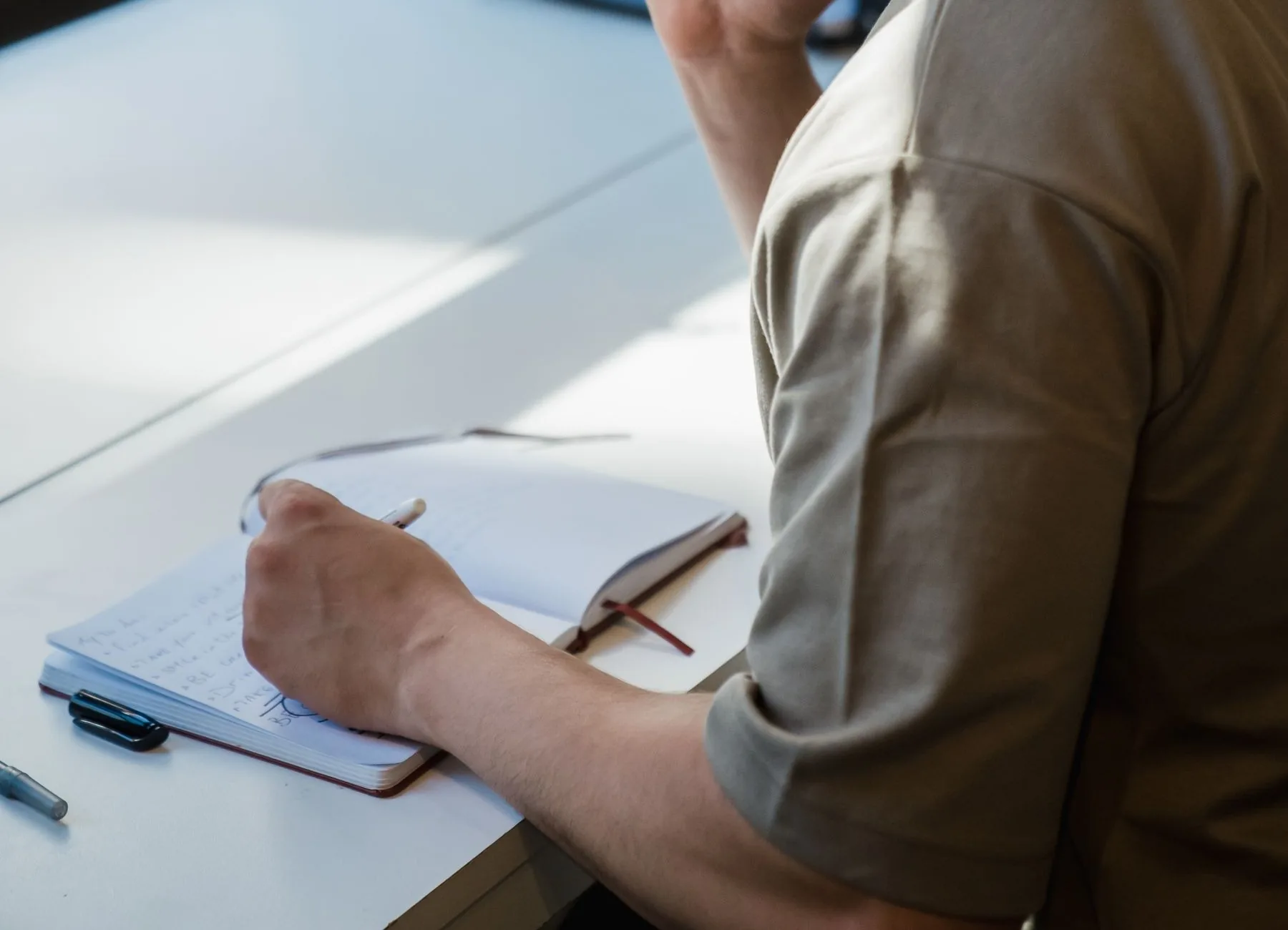 A person holds a pen over an open notebook on a desk.