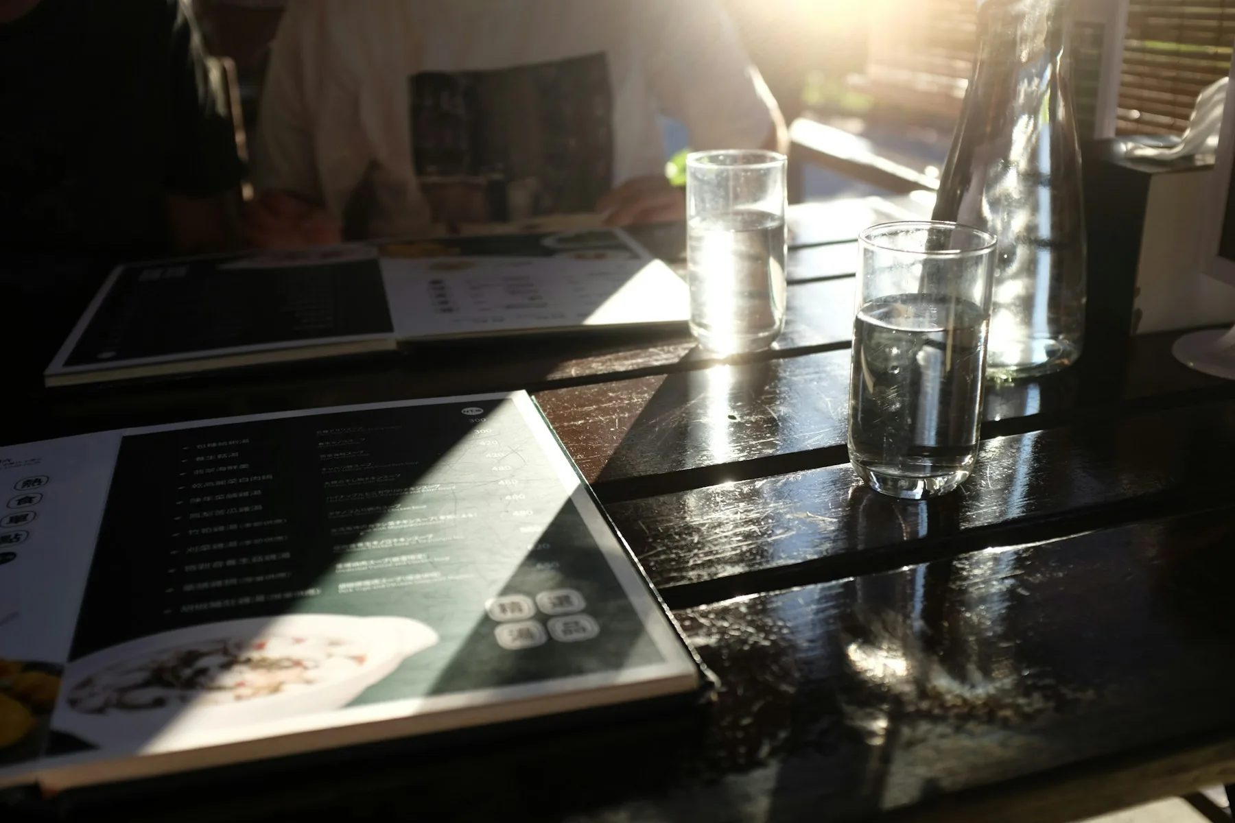 Two menus and water glasses on a sunlit restaurant table.