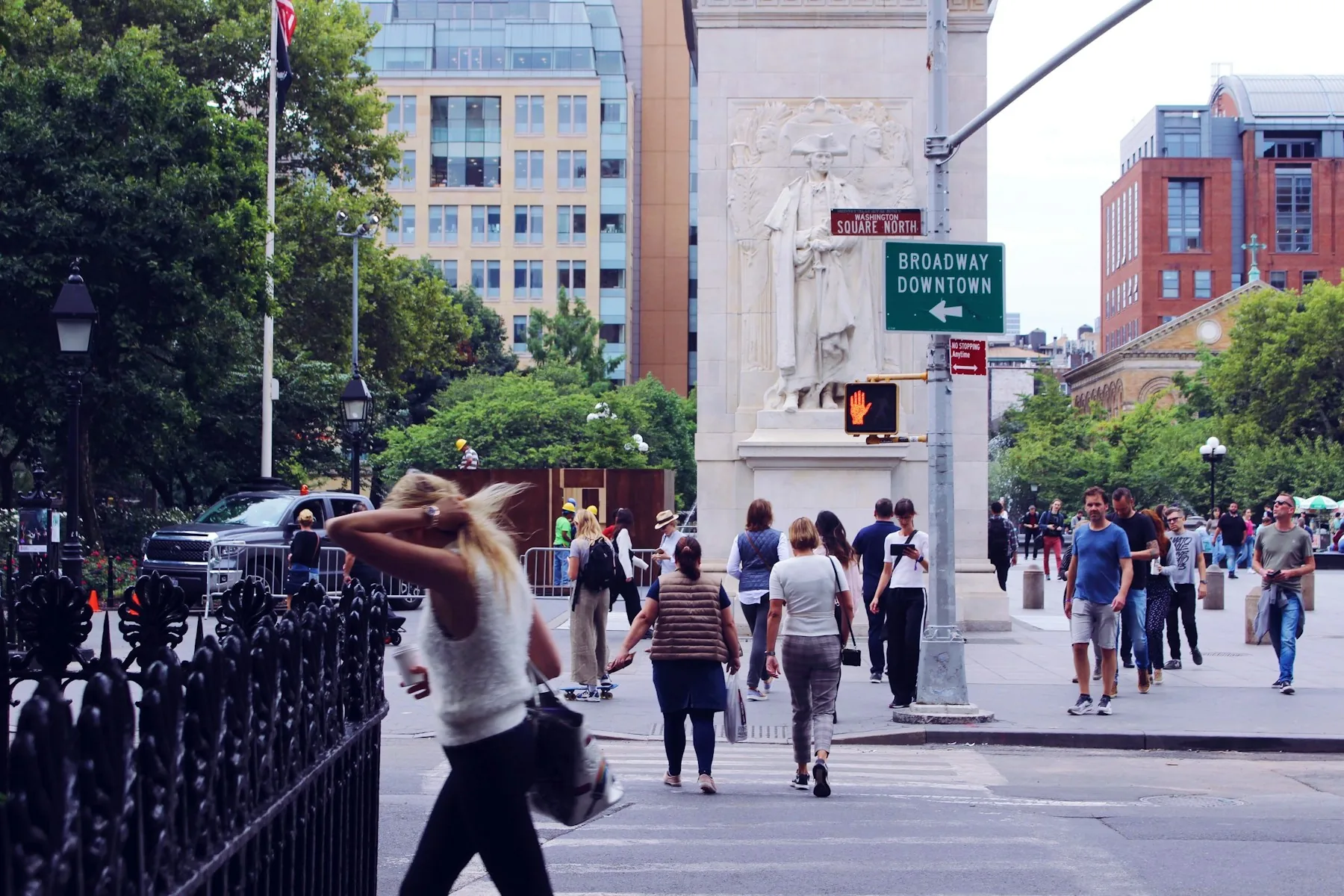 Pedestrians cross a street beside the Washington Square Park fence and arch in New York City.